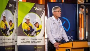 Man with white shirt and silver glasses standing at podium addressing audience